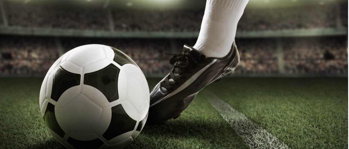 Imagem de uma pessoa usando chuteiras e chutando uma bola de futebol