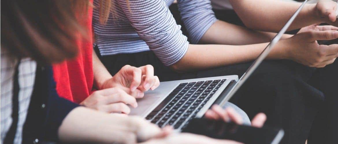 Imagem de diversas pessoas participando de uma reunião. Uma delas está mexendo em um laptop, enquanto outros mexem no celular