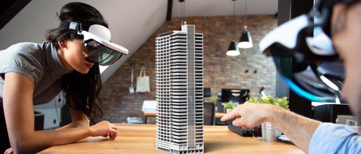 Jovem com óculos de realidade virtual observa a maquete de um edifício