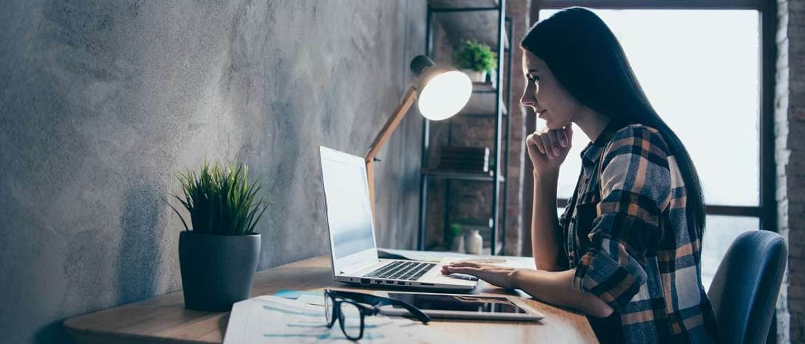 Mulher sentada em um escritório olha para a tela de seu computador enquanto trabalha