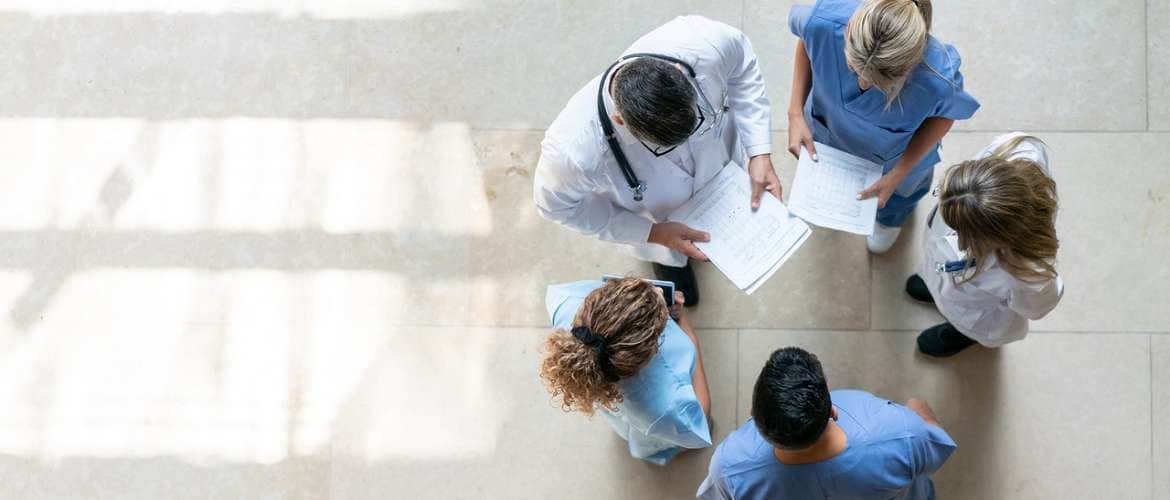 Imagem de uma reunião em círculo de 5 profissionais de saúde em um hospital
