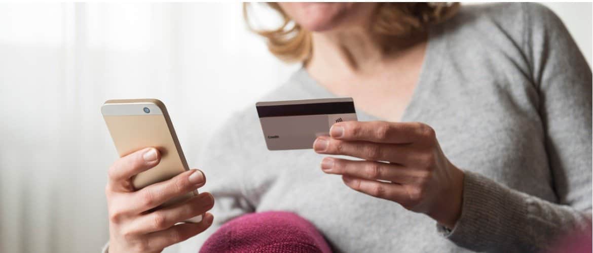 Mulher segura um cartão de crédito com uma mão e o telefone celular com outra mão para fazer um pagamento digital