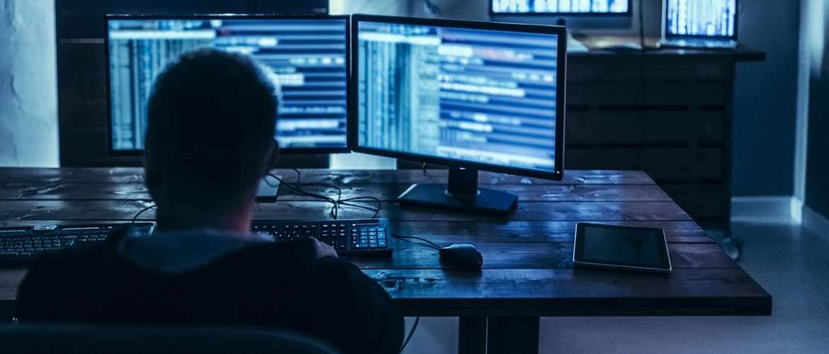 Imagem de uma pessoa observando duas telas de computador em um cenário escuro