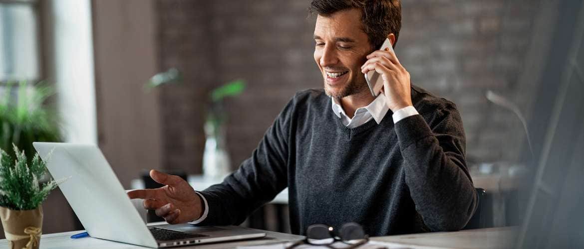 Imagem de um executivo conversando no celular enquanto trabalha no laptop