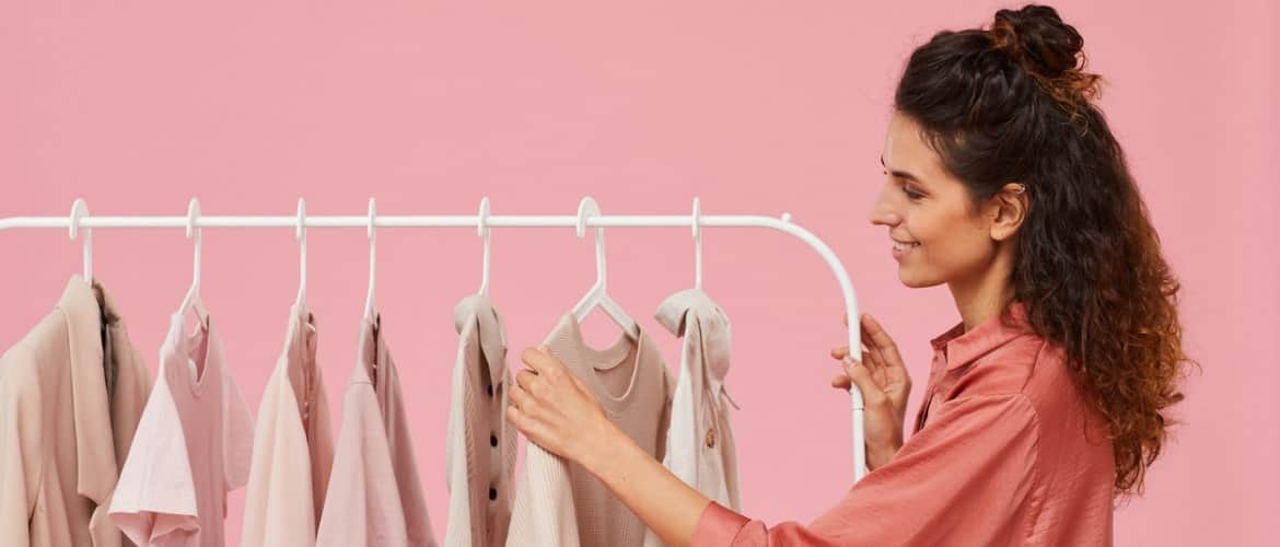 Imagem de mulher escolhendo roupas em uma arara com cabides_indústria têxtil