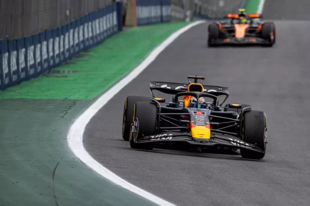 Carro de Fórmula 1 em alta velocidade na pista durante uma corrida, com outro carro ao fundo, mostrando ação e velocidade.