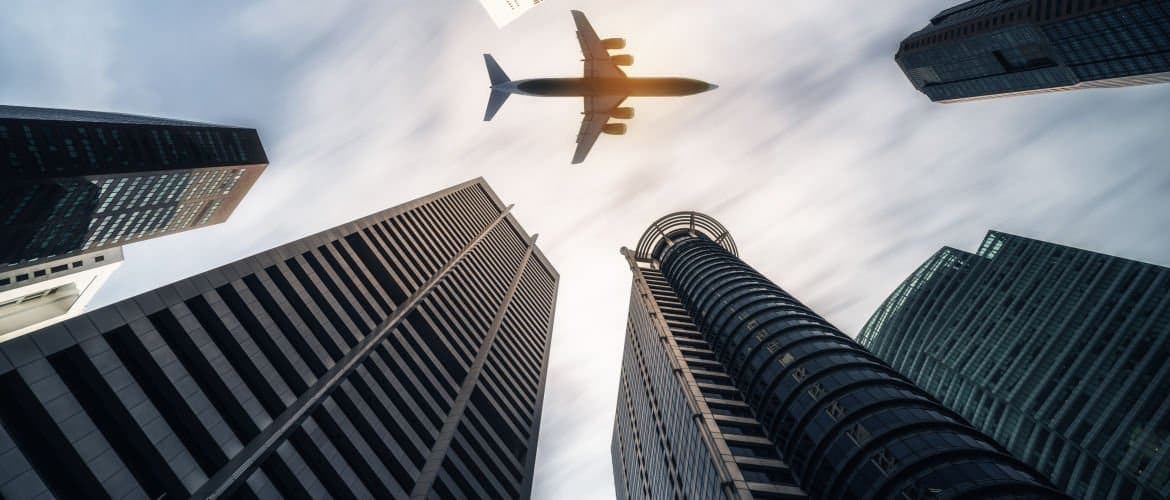 Avião passando por vários prédios em um céu com nuvens