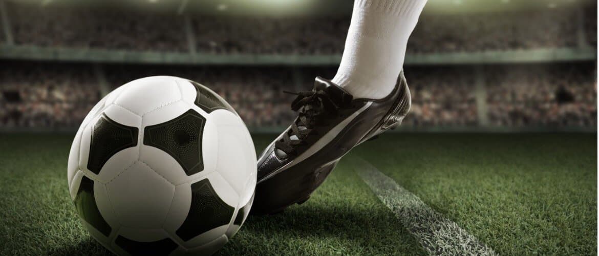 Imagem de uma pessoa usando chuteiras e chutando uma bola de futebol