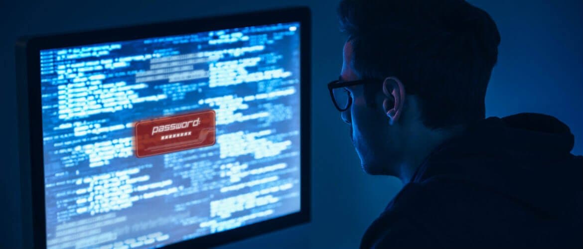 Imagem de um homem olhando para a tela de um computador. Há um aviso na tela com a palavra "senha" escrito.