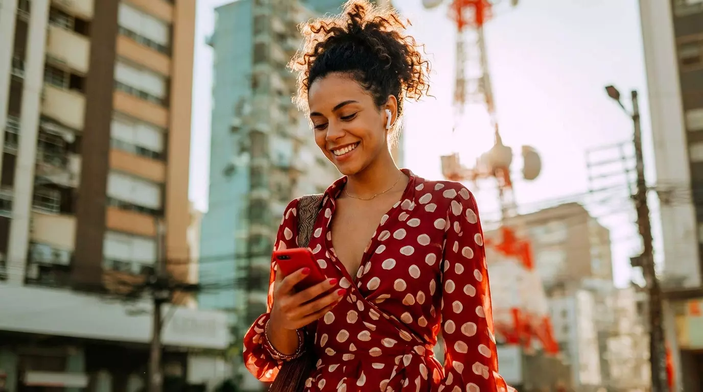 Jovem mulher usando celular em uma rua movimentada, simbolizando conexão e acessibilidade de rede móvel no cotidiano urbano.