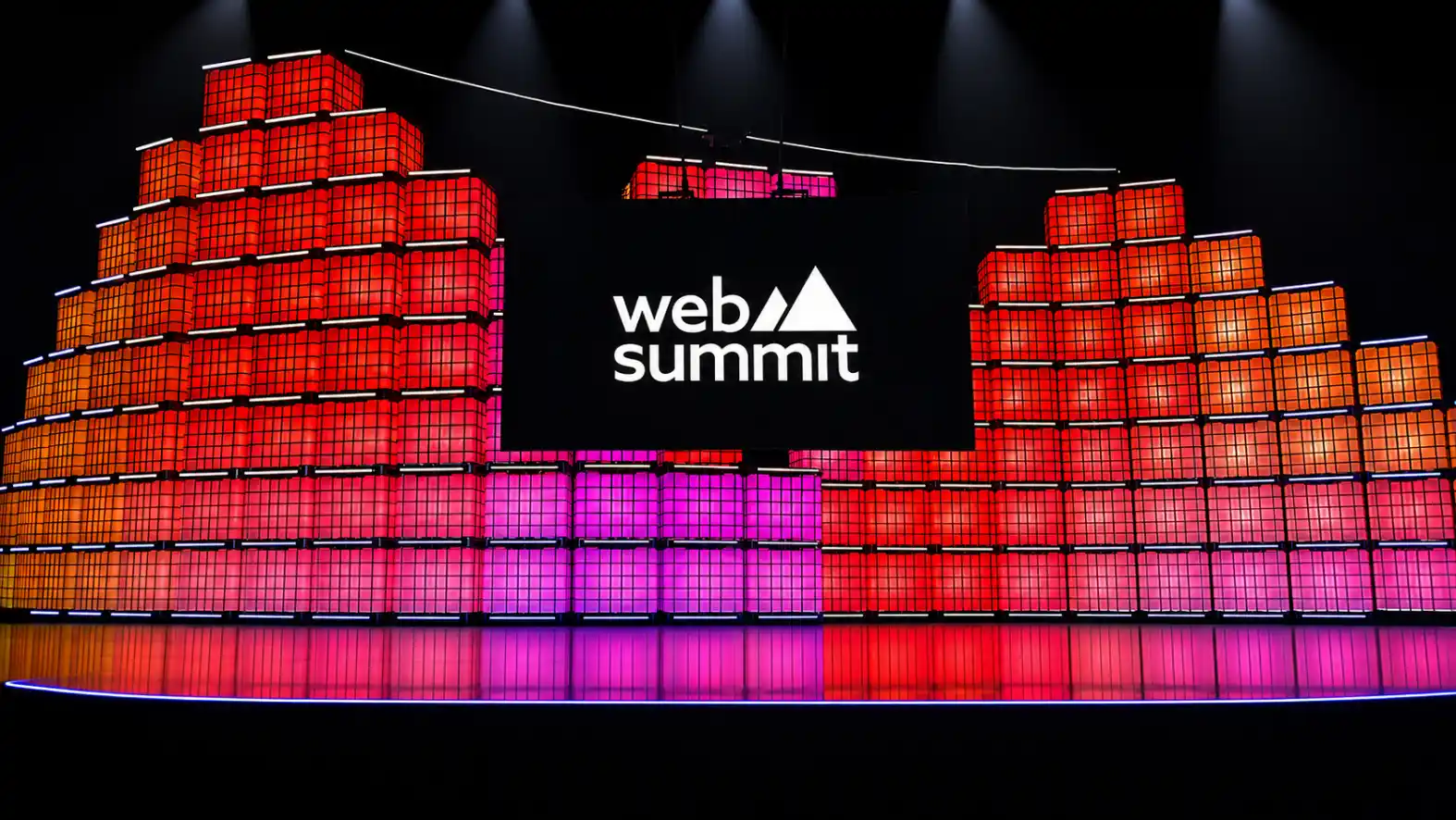 Fachada iluminada do Web Summit com o logo “web summit” ao centro, cercada por estruturas em cubos com luzes coloridas, em um cenário de evento de fintechs e pagamentos digitais