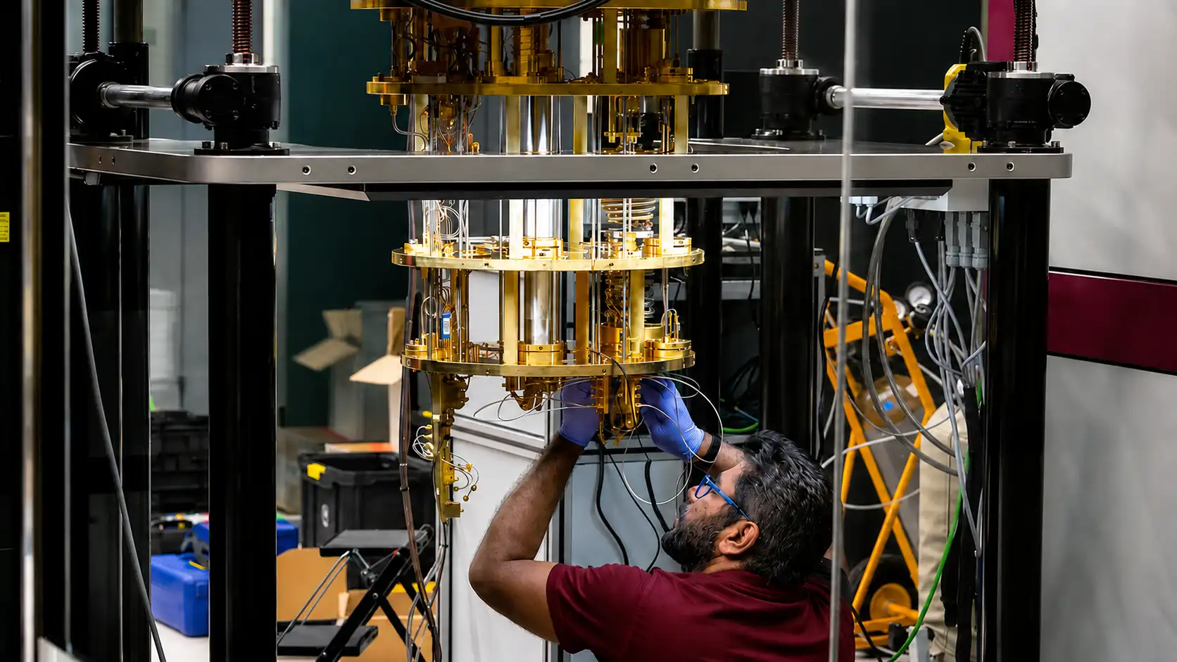 Técnico ajusta um maquinário quântico com componentes metálicos e cabos em um ambiente de pesquisa, com foco em tecnologia associada à IBM e computação quântica.
