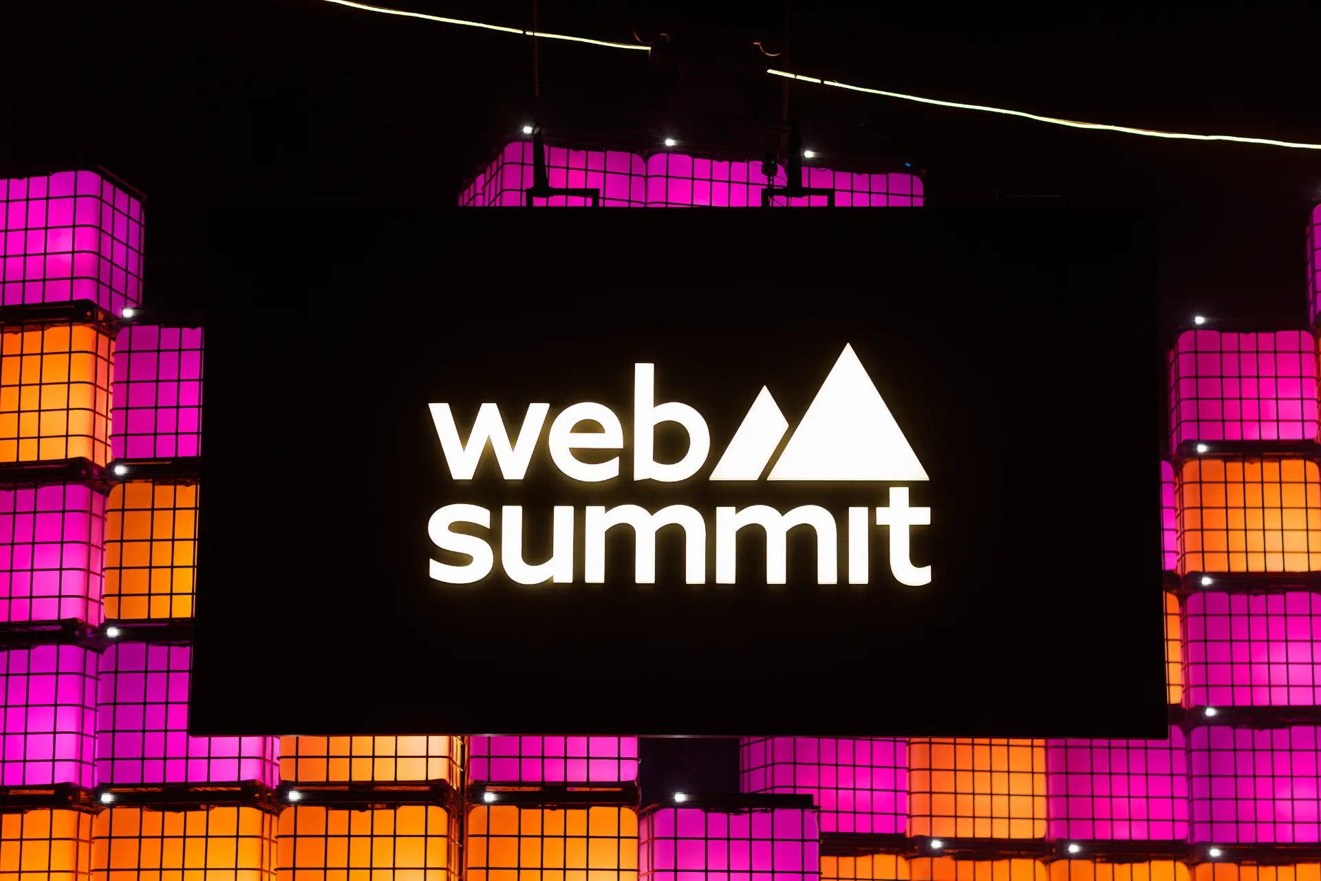 Placa iluminada do evento Web Summit no Rio de Janeiro, com luzes roxas e laranja ao redor de um painel com o logo web summit