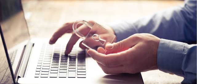 Mãos de um homem segurando um cadeado enquanto digita no teclado de um notebook