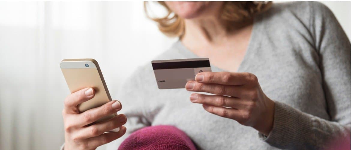 Mulher segura um cartão de crédito com uma mão e o telefone celular com outra mão para fazer um pagamento digital