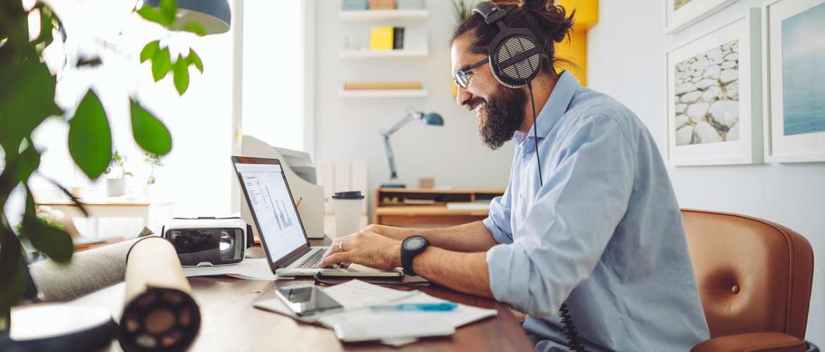 Homem realiza trabalho em casa, a partir de seu laptop, enquanto utiliza um fone de ouvido