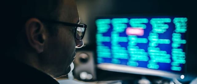 Imagem de um homem olhando para uma tela com códigos de programação