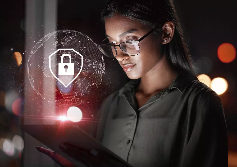 Mulher usando óculos observa um dispositivo móvel com uma representação digital de segurança, símbolo de criptografia e proteção na estratégia nacional de cibersegurança.a