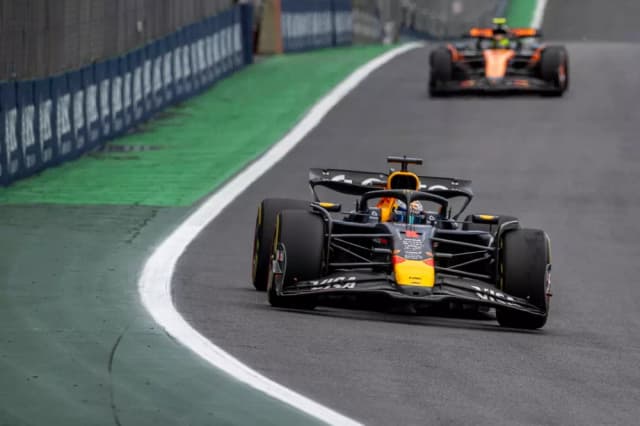 Carro de Fórmula 1 em alta velocidade na pista durante uma corrida, com outro carro ao fundo, mostrando ação e velocidade.
