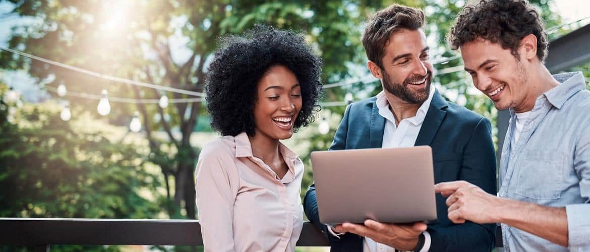 Três executivos - uma mulher negra e dois homens brancos - acessam a internet em um notebook