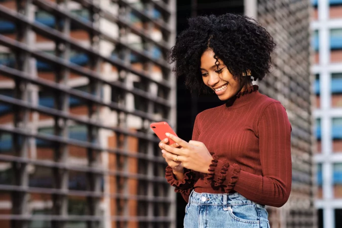 Mulher sorrindo usando blusa vermelha usando a rede móvel do celular com fundo de uma estrutura de rede, ilustrando a importância da observabilidade de rede corporativa.