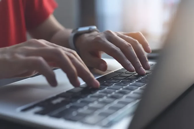 Pessoa digitando em um notebook, foco nas mãos, com iluminação suave ao fundo
