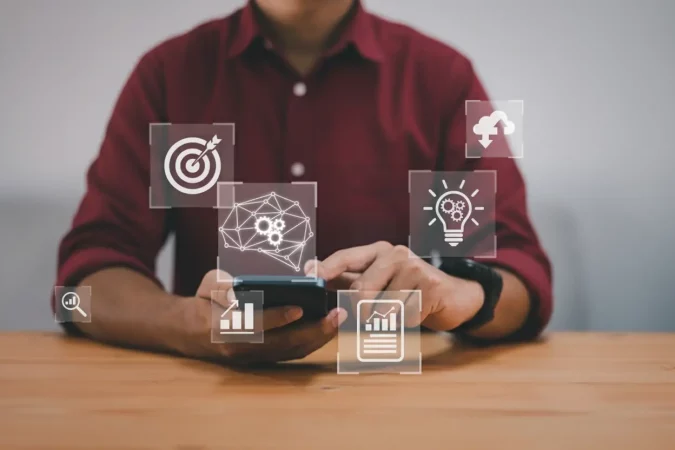	
Pessoa usando smartphone para gestão e governança de dados, com ícones de metas, gráficos, tecnologia, inteligência artificial e nuvem digital.