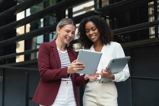 Duas mulheres empresárias discutindo sobre modernização de dados na era da inteligência artificial, utilizando tablets, em ambiente de negócios.